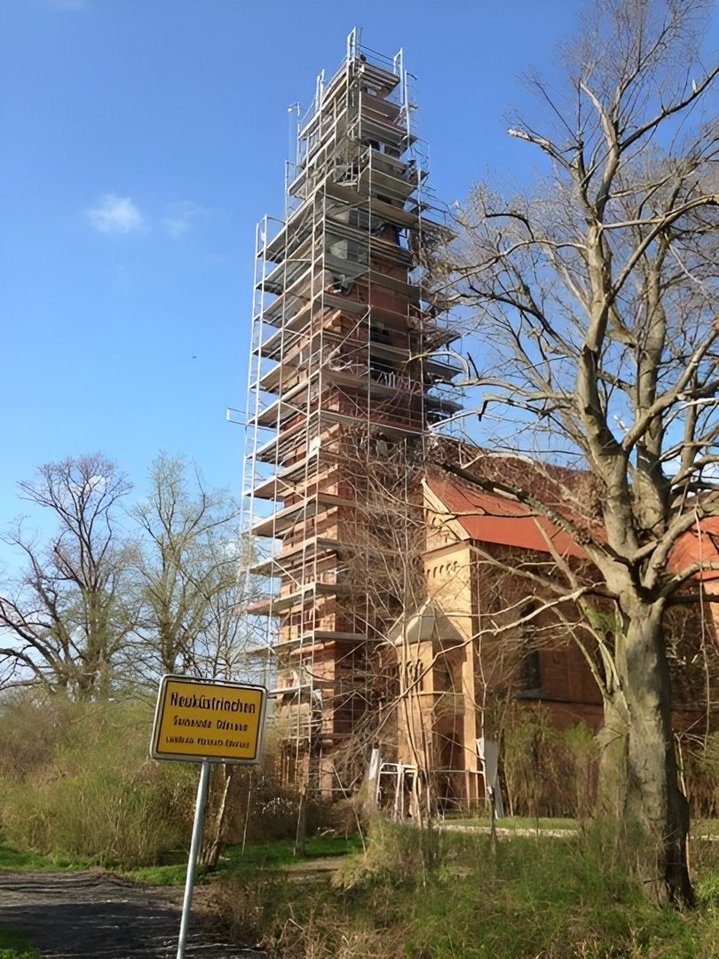 Kirchturm, der vor einem Ortsschild steht mit Gerüstbau